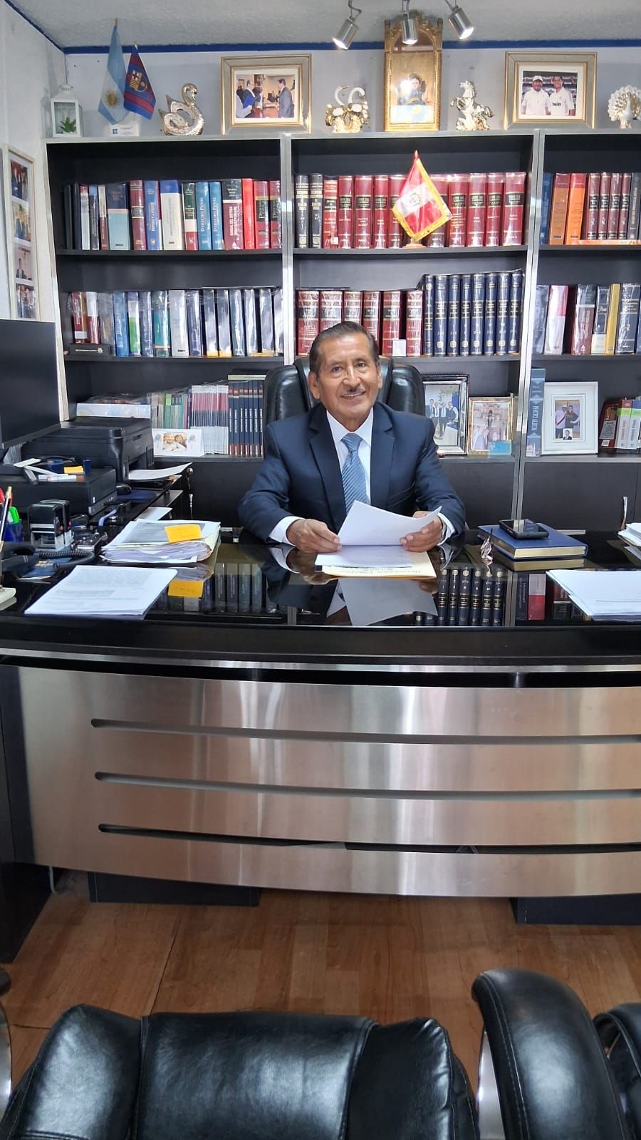El Dr. Severino Saire revisando documentos en su escritorio, frente a la biblioteca de su despacho